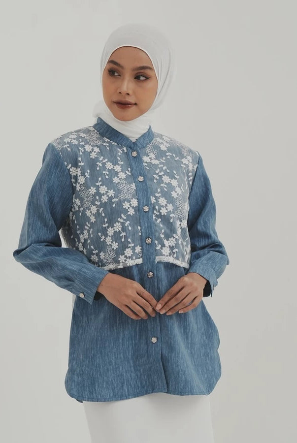 Woman wearing a blue denim shirt with floral embroidery by Tunique on a plain background