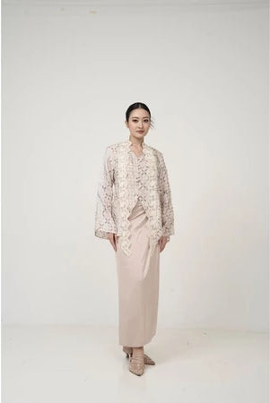 Woman wearing a patterned kebaya by Kartinis Label and beige skirt on a white background