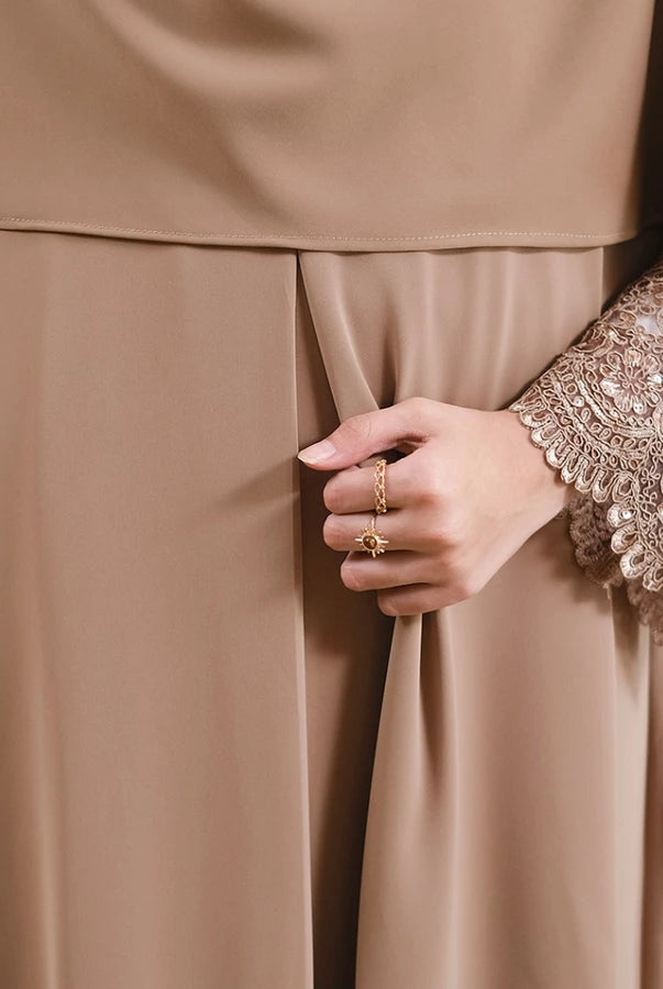Close-up of a person wearing a beige abaya with intricate lace detailing on the sleeves by Tubita.