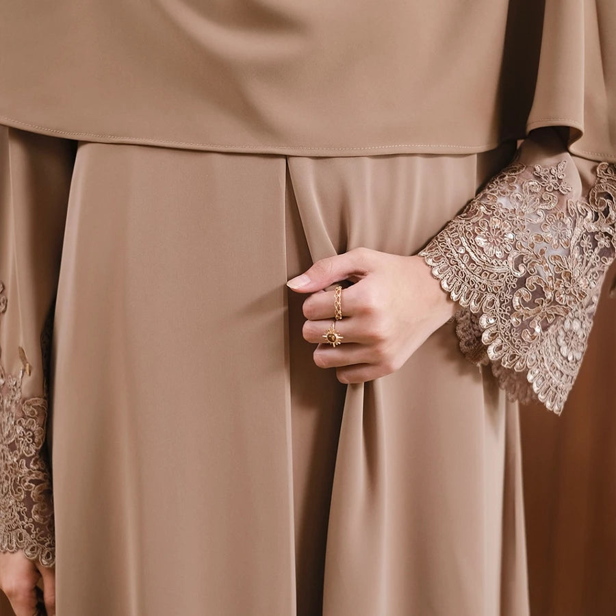 Close-up of a person wearing a beige abaya with intricate lace detailing on the sleeves by Tubita.