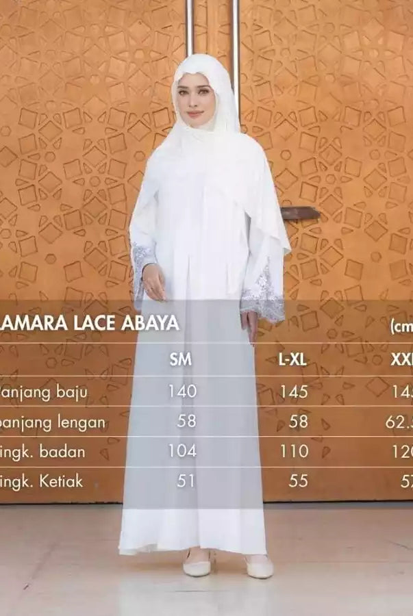 Woman wearing a white lace abaya with size chart against an orange patterned wall.