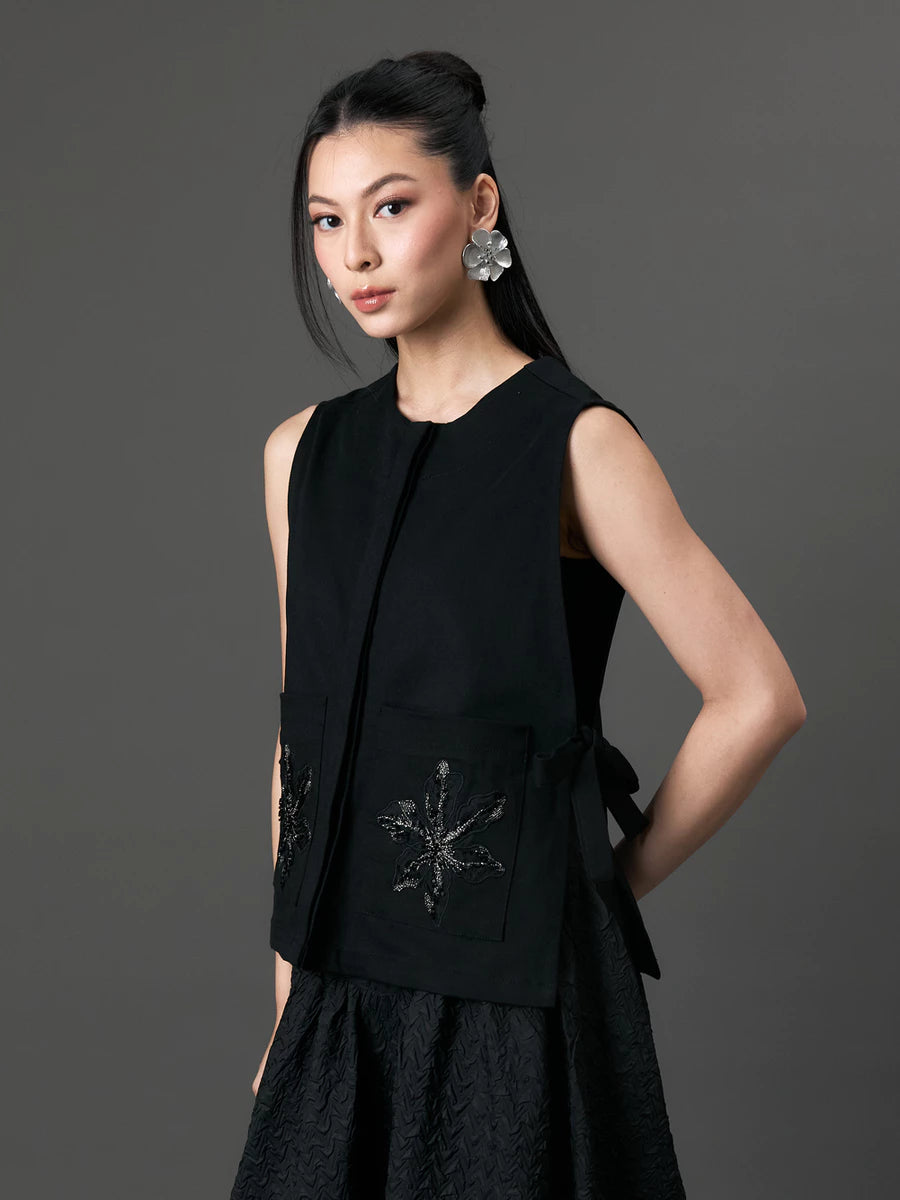 Woman wearing a black sleeveless vest by Studio Tui with decorative elements on a gray background