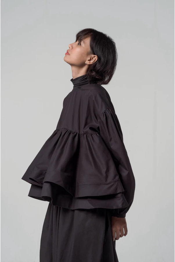 Person wearing a black layered blouse by Yestoday and skirt set against a plain background