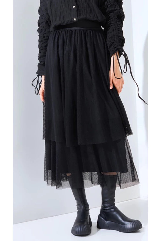 A person wearing a layered black skirt by Yestoday with a elastic waistband and black boots. The skirt has a solid color and appears to be made of a smooth fabric with a flared design.