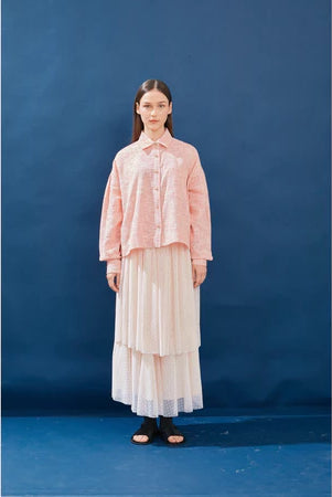 Woman wearing a pink blouse and pink layered skirt by Yestoday against a blue background