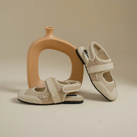 Pair of cream flat shoes with a decorative element by Dianable on a beige background