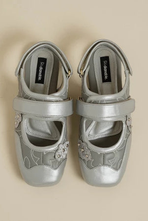 Pair of silver flat shoes with decorative elements by Dianable on a beige background