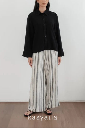 Person wearing a black shirt and striped pants standing against a white wall with 'kasyalia' branding.