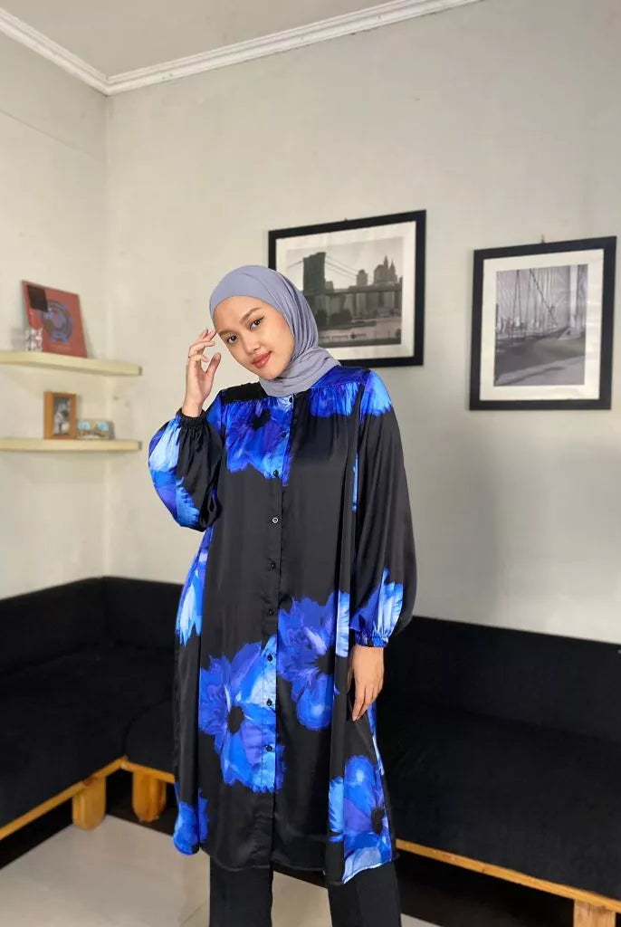 A person wearing a black tunic with blue floral print. The tunic has long sleeves and reaches mid-thigh.
Seorang wanita memakai tunik berwarna hitam dengan aksen print bunga berwarna biru.