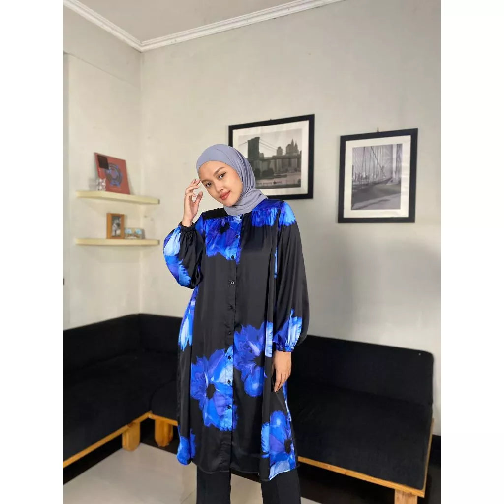 A person wearing a black tunic with blue floral print. The tunic has long sleeves and reaches mid-thigh.
Seorang wanita memakai tunik berwarna hitam dengan aksen print bunga berwarna biru.