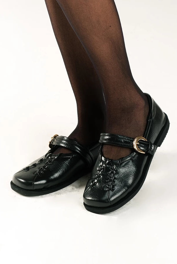 Black leather flat shoes by Cekhas with buckles worn by a person on a white background