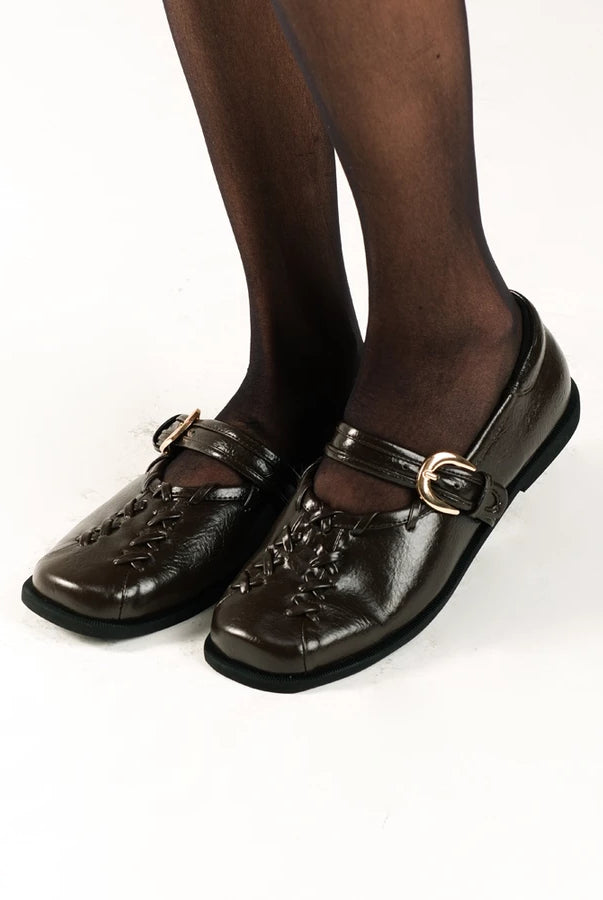 Brown flat shoes by Cekhas with buckles worn by a person on a white background