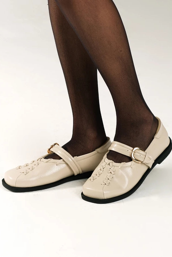 Beige leather falt shoes by Cekhas with black soles worn with black tights on a white background