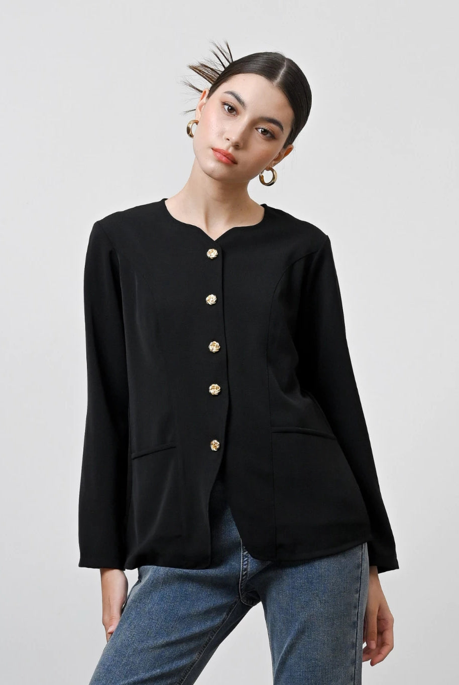 A woman wearing a black long-sleeved blouse with gold front buttons by Kasa Heritage, paired with blue jeans.