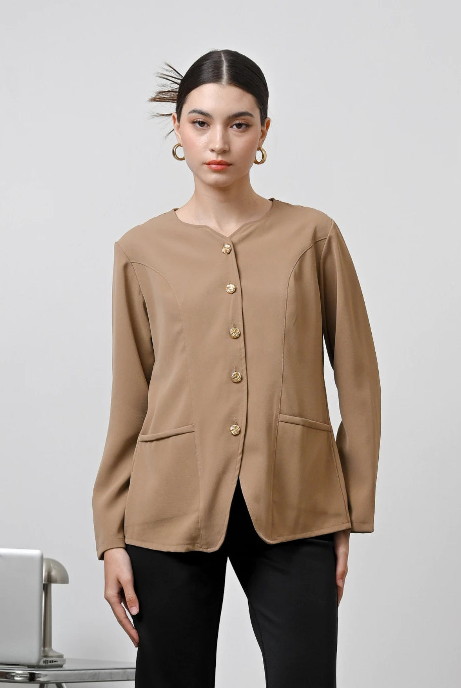 A woman wearing a brown long-sleeved blouse with gold front buttons by Kasa Heritage, paired with blue jeans.