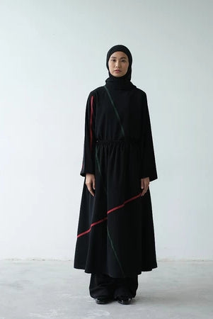 A person wearing a black Rashawl Levy pleated patch blouse with a hood, featuring a simple design with possibly pleats on the left hand.