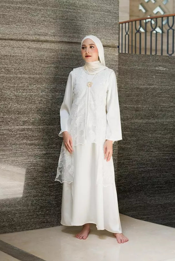 Woman in a white dress by Tunique standing against a textured wall.