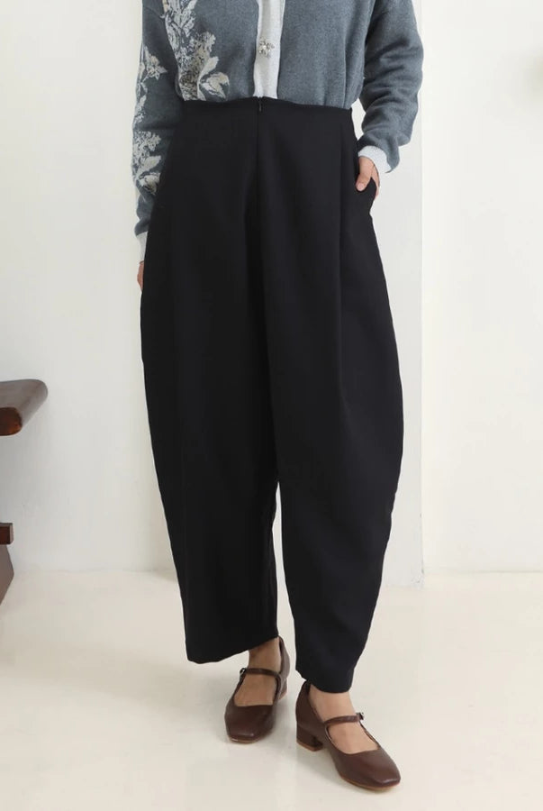 Person wearing black wide-leg pants by Hijabchic with a light gray cardigan and brown shoes in a minimalistic setting.