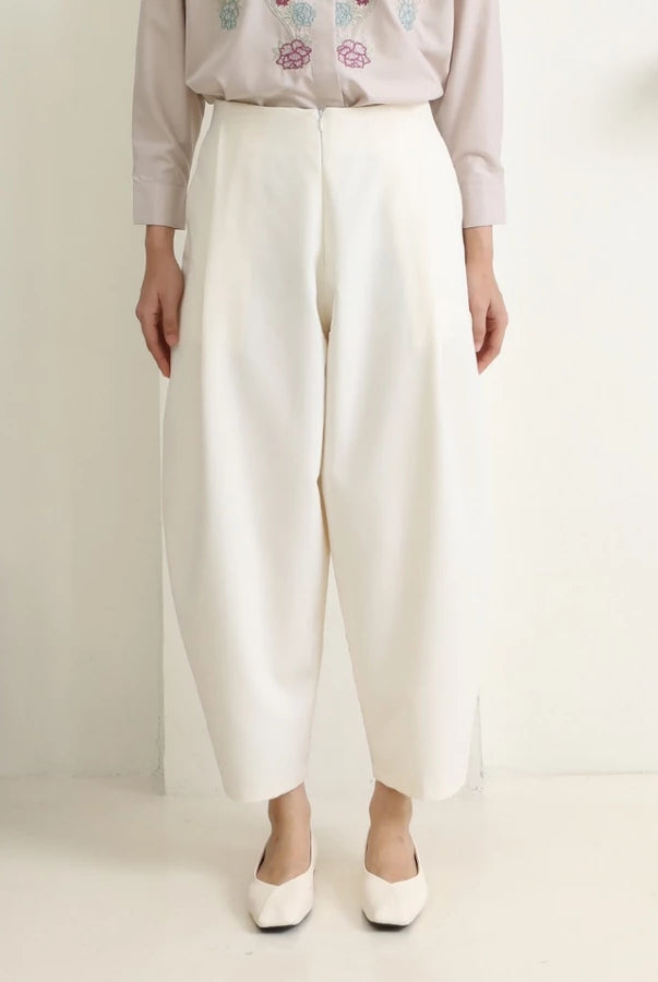 Person wearing white wide-leg pants by Hijabchic and a light-colored top with floral embroidery on a plain background