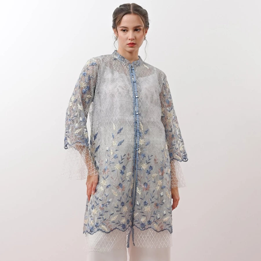 Woman wearing a blue floral embroidered tunic by Holy Peony on a white background.
Wanita mengenakan tunik berhias bordir bunga berwarna biru dari Holy Peony dengan latar belakang putih.