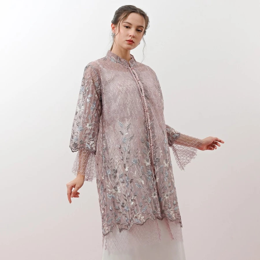 Woman wearing a lilac floral embroidered tunic by Holy Peony against a white background.
Seorang wanita mengenakan tunik bermotif bunga ungu muda dengan bordir bunga dari Holy Peony di latar belakang putih.