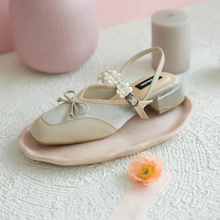 Beige mules sandal with decorative bow and flower by Dianable on a white surface with pink and gray background