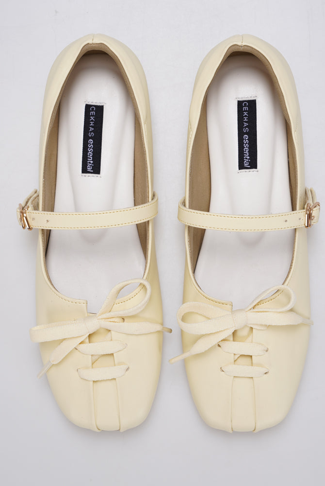 A pair of butter yellow Mary Jane ballet flatshoes by Cekhas with matching ribbon bows and small gold-tone buckle details, displayed on a light gray background.
