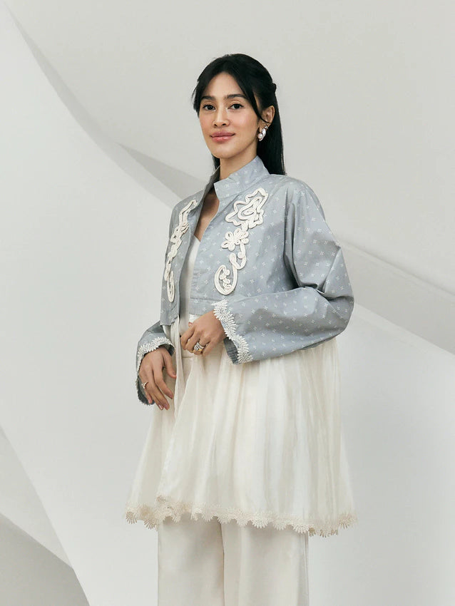 Woman wearing a gray embroidered jacket by Studio Tui with white details on a plain background