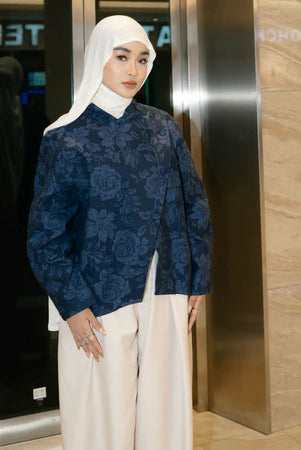 Woman in a navy blue patterned top by Haidee Orlin and white hijab standing in an elevator.