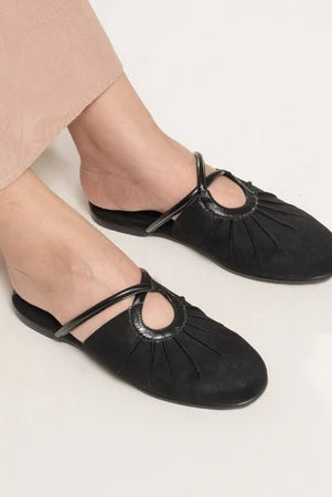 Black flat shoes from Dianable worn with beige pants on a light background