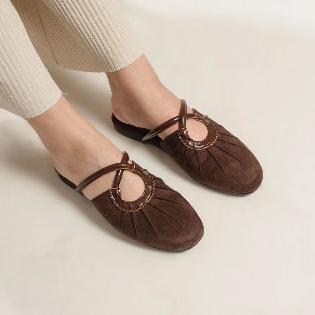 Brown flat shoes with a decorative strap from Dianable worn by a person on a light background