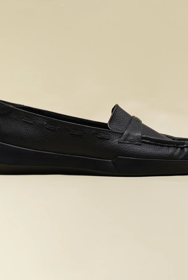 A single black leather slip-on loafer flatshoes by Cekhas with a textured pebbled upper and a chunky black platform sole, shown in profile against a solid beige background.