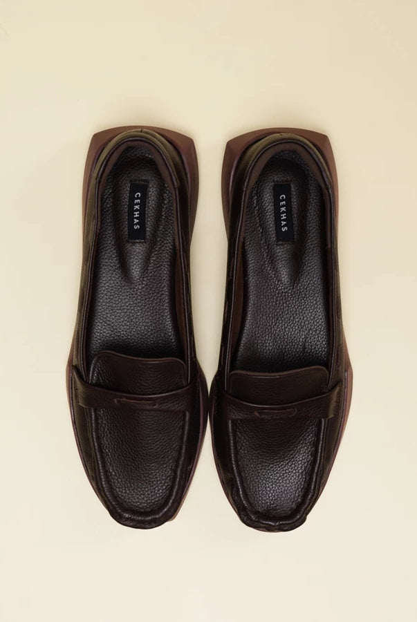 A pair of dark brown leather penny loafers flatshoes with a pebbled texture, shown from a top-down view on a light cream background. The brand name 'Cekhas' is visible on the insoles.