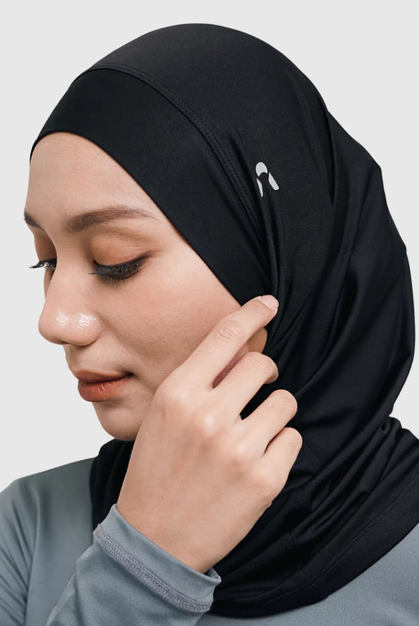 Woman wearing a black sport hijab by HIA on a light gray background