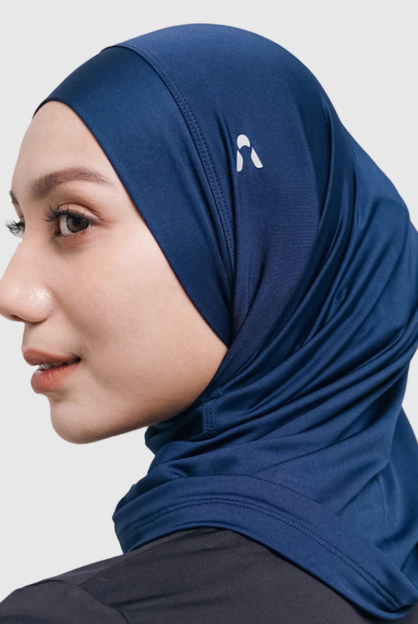 Woman wearing a navy sport hijab with a logo by HIA on a light gray background
