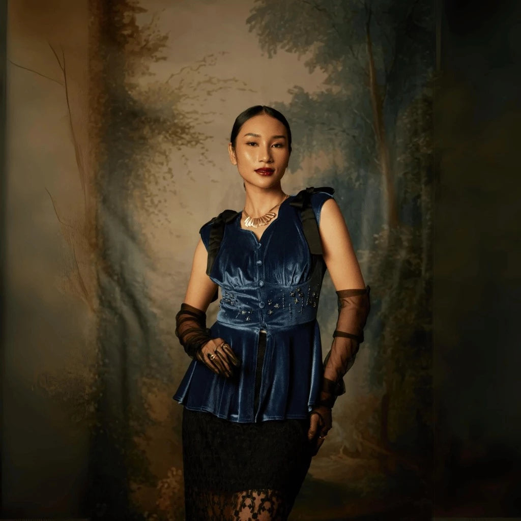 A woman wearing a sleeveless, flared, mid-night blue colored top by Kartinis Label with velvet material and decorative elements on the shoulders and waist.