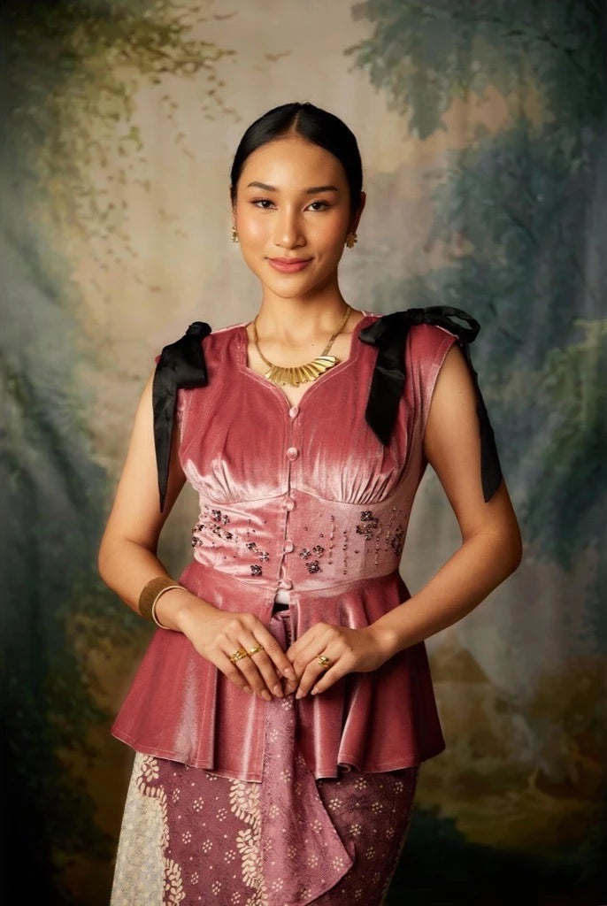 A woman wearing a sleeveless, flared, mauve colored top by Kartinis Label with velvet material and decorative elements on the shoulders and waist.