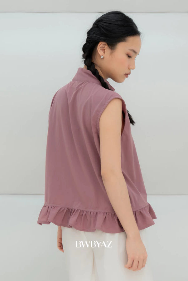 A woman wearing a sleeveless dusty rose ruffled vest by BWBYAZ and white pants, shown from a side-back angle against a clean white studio background. The brand name BWBYAZ is printed on the white pants.