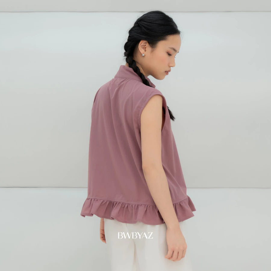 A woman wearing a sleeveless dusty rose ruffled vest by BWBYAZ and white pants, shown from a side-back angle against a clean white studio background. The brand name BWBYAZ is printed on the white pants.