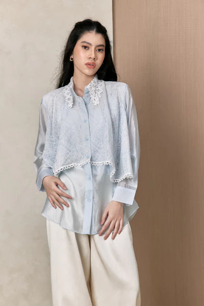 Woman wearing a light blue shirt with lace details by Studio Tui against a beige background