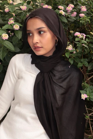 A woman wearing a black pashmina scarf, likely a pashmina, with a garden background.