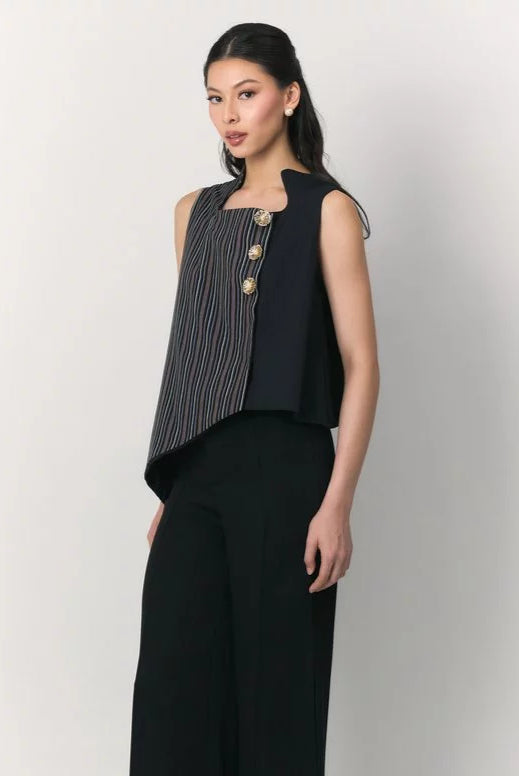 A woman modeling a sleeveless navy black top by Studio Tui with a vertically striped front panel and three gold-tone decorative buttons, paired with black wide-leg pants, against a plain light gray studio background.
