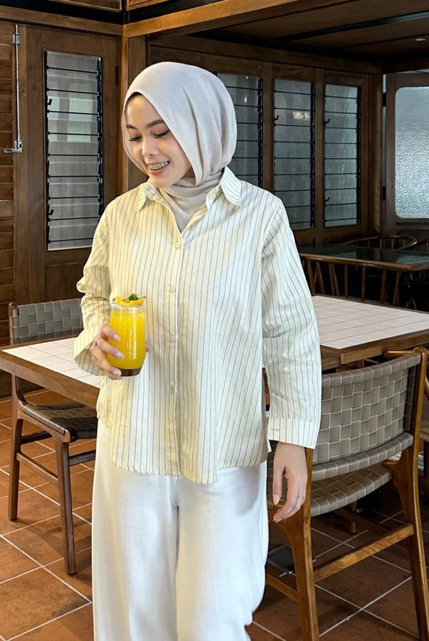 Woman wearing light yellow striped shirt by Renaette holding a glass of orange juice in a restaurant setting