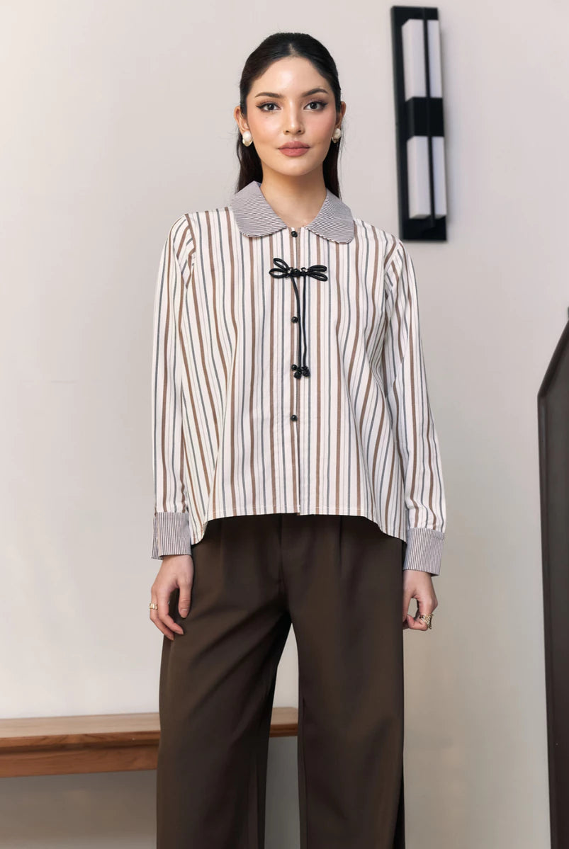 Woman wearing a striped shirt with a collar by Studio Tui and brown pants in an indoor setting.