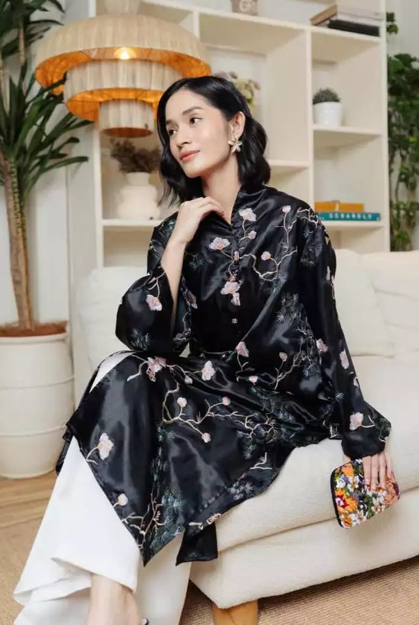 Woman in a black floral tunic by Haidee Orlin sitting on a white couch in a home setting.
Seorang wanita mengenakan tunik bermotif bunga berwarna hitam karya Haidee Orlin sedang duduk di sofa putih di dalam sebuah rumah.