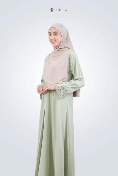 Woman wearing a light green abaya with a matching hijab on a white background, featuring the brand 'TUBITA'.