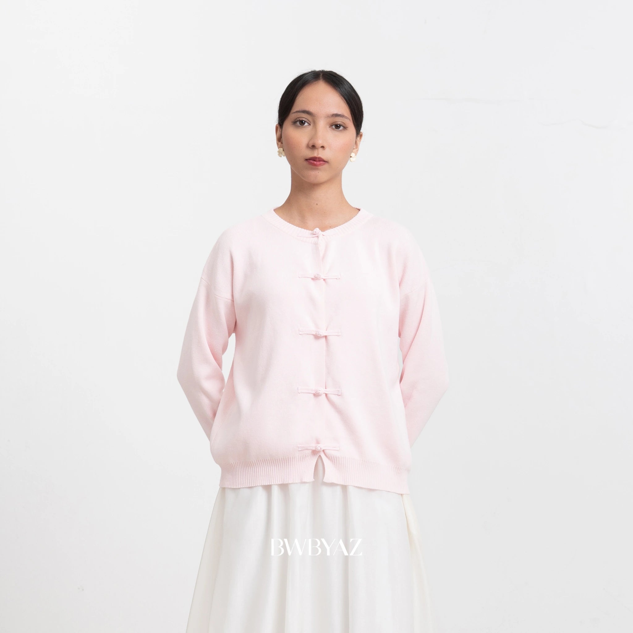 Woman wearing a light pink cardigan and white pants on a white background with 'BWBYAZ' branding.