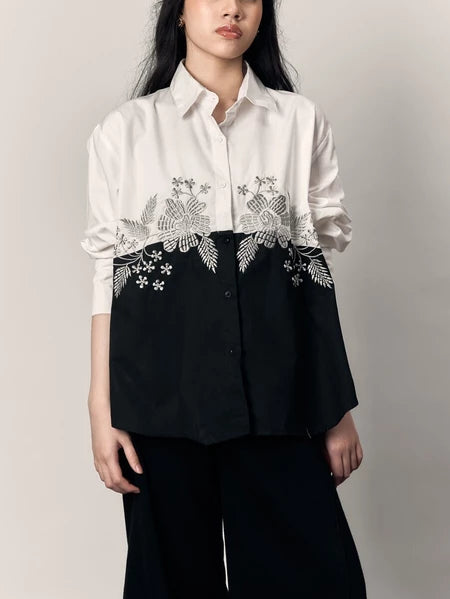Person wearing a black and white shirt with floral embroidery by Studio Tui on a plain background