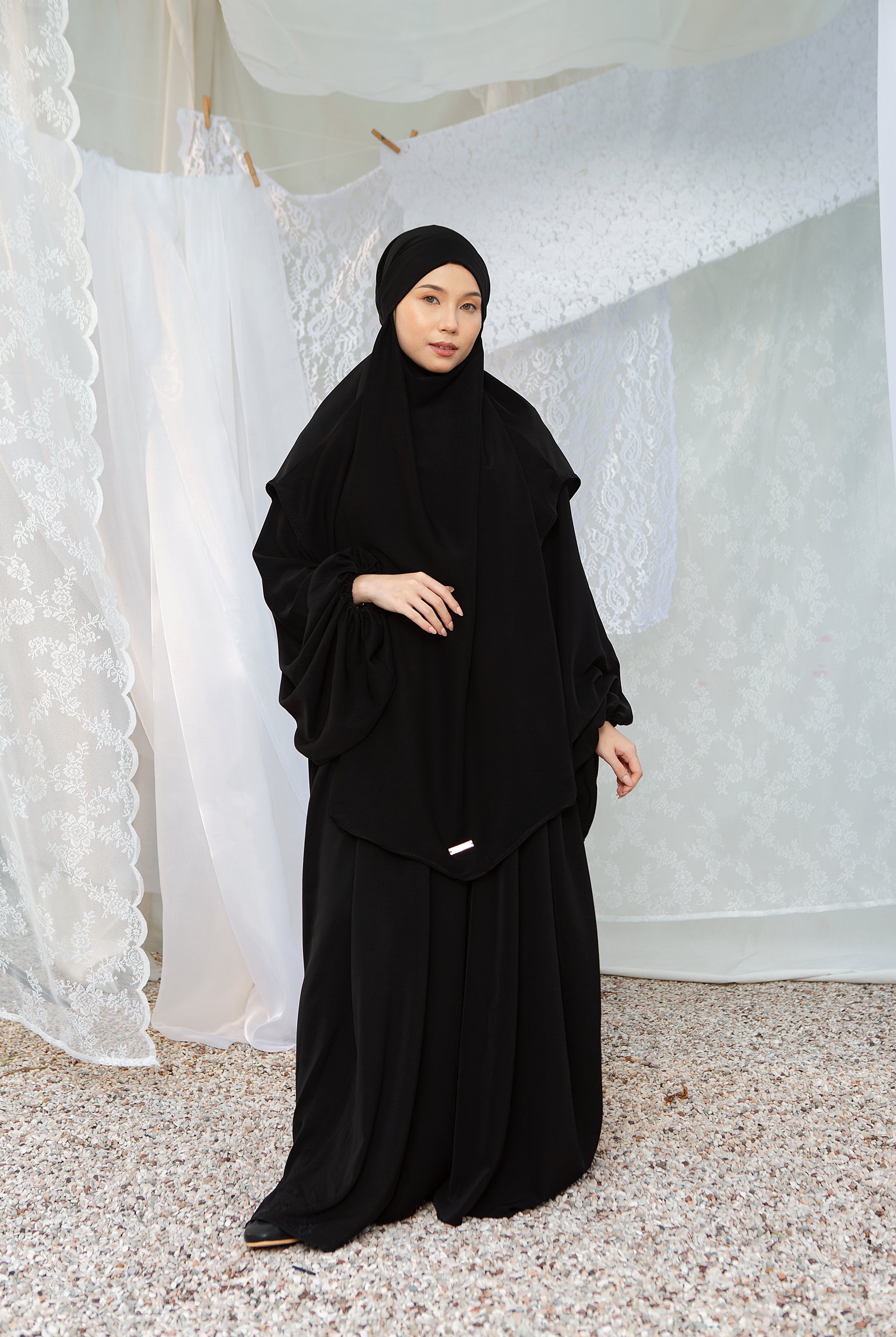 A woman wearing a black abaya set with a matching headscarf by Lozy Hijab, standing indoors.