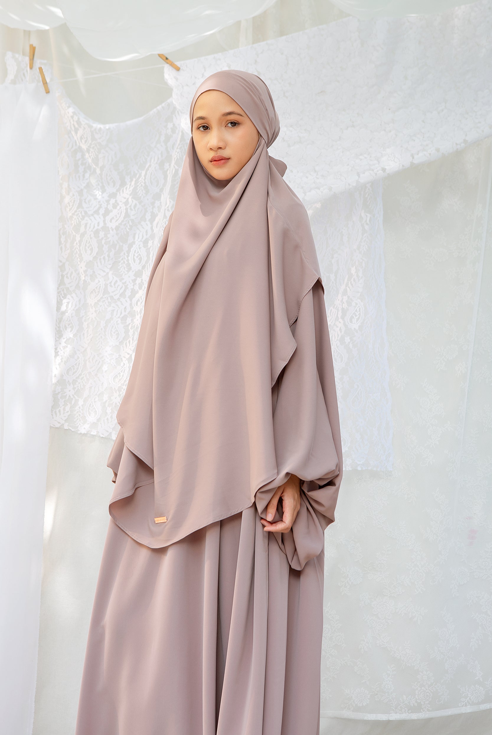 A woman wearing a grey cream abaya set with a matching headscarf by Lozy Hijab, standing indoors.